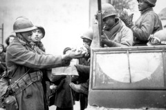 Two smiling French soldiers fill the hands of American soldiers with candy, in Rouffach, France, after the closing of the Colmar pocket.